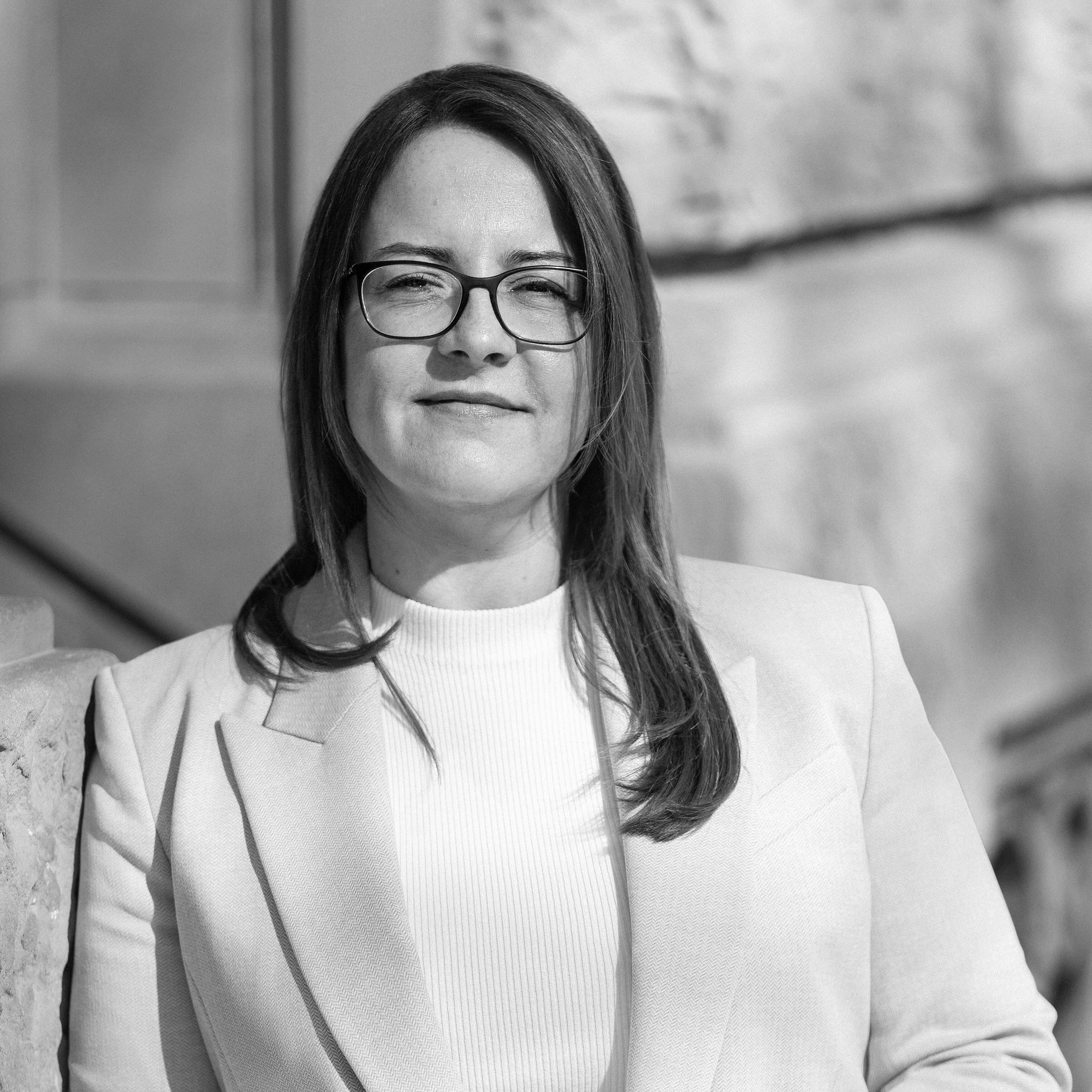 Rechtsanwältin Melanie Freiin von Neubeck in hellem Blazer, steht selbstbewusst vor einem historischen Gebäude und blickt in die Kamera.