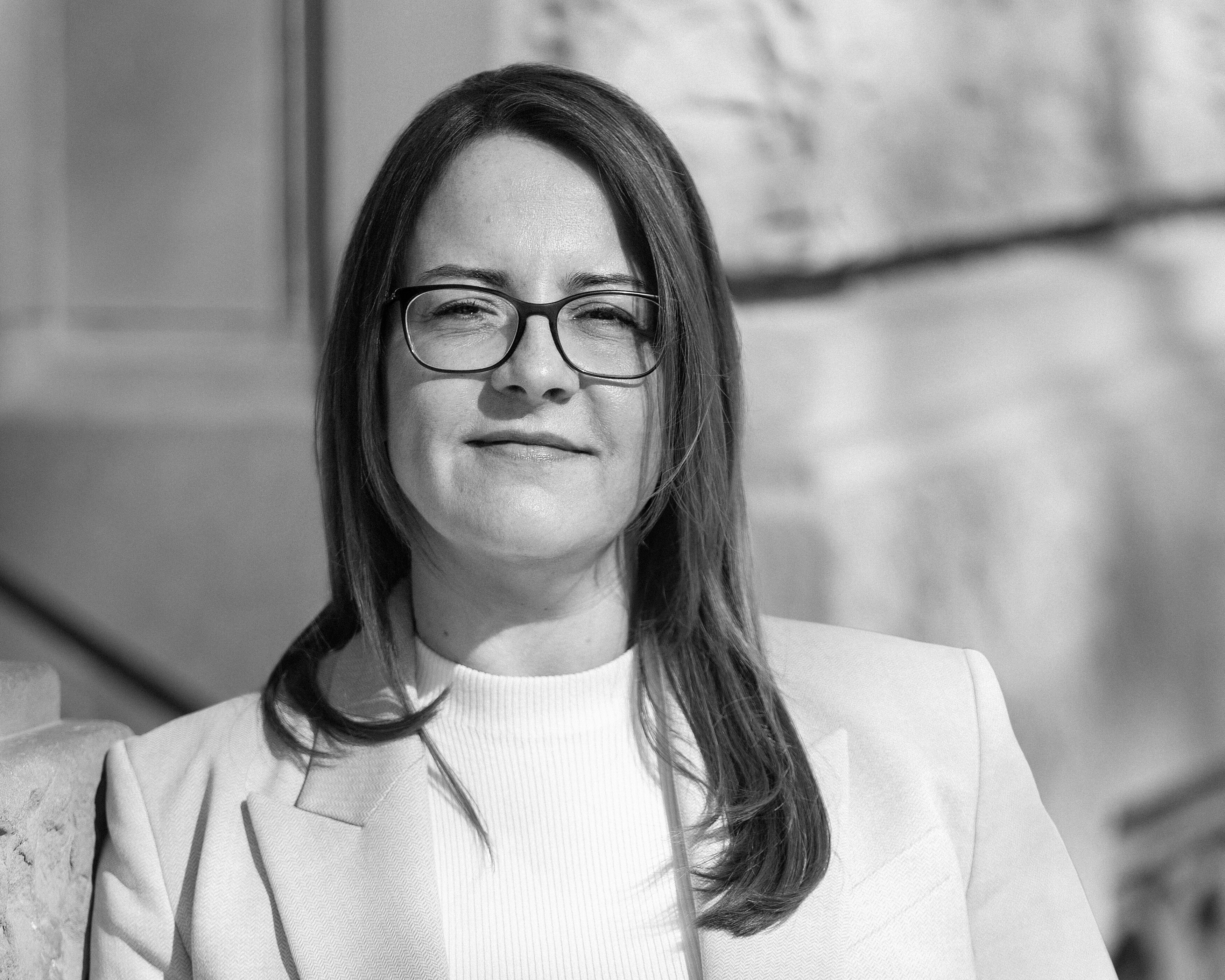 Rechtsanwältin Melanie Freiin von Neubeck in hellem Blazer, steht selbstbewusst vor einem historischen Gebäude und blickt in die Kamera.