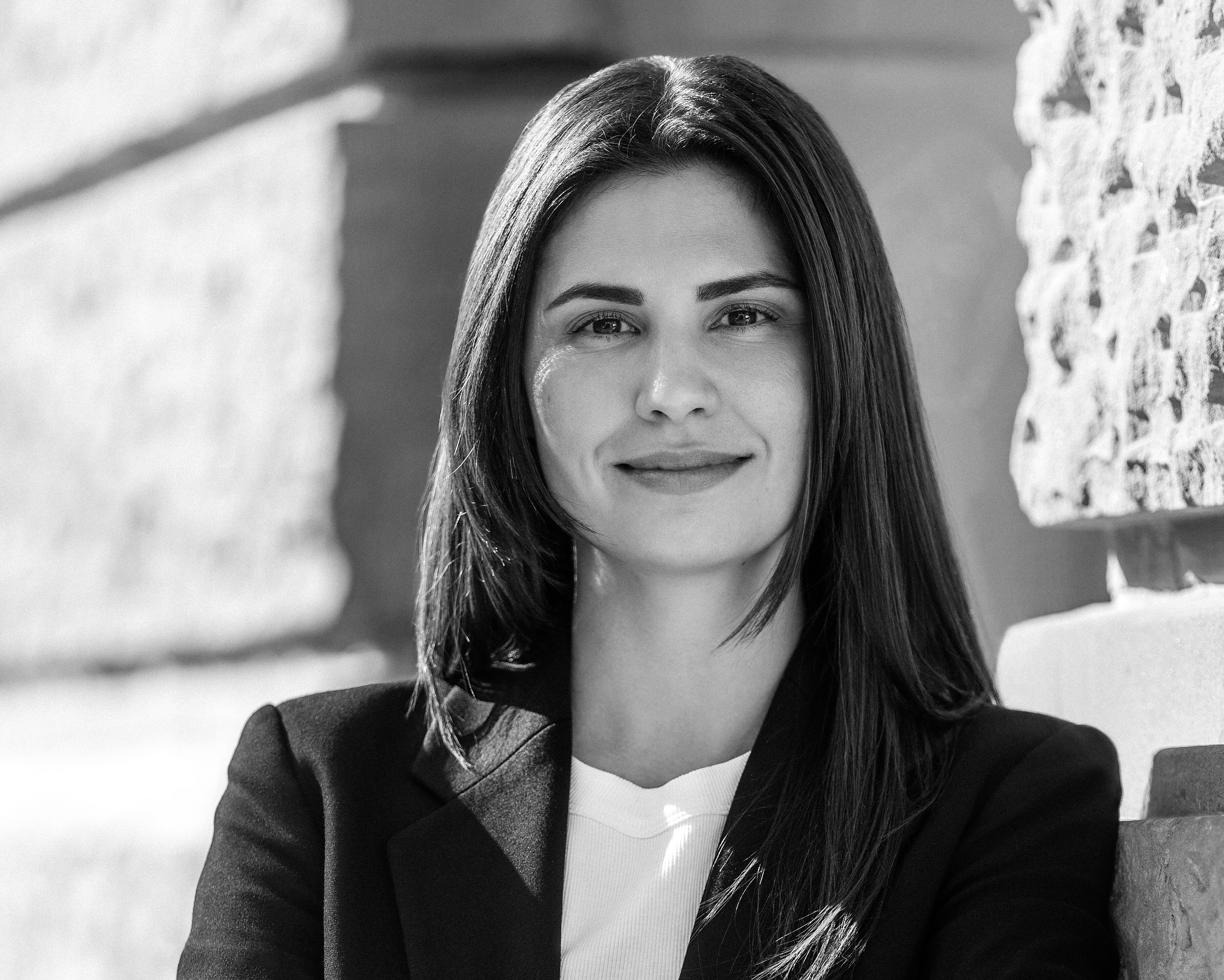 Rechtsanwältin Nadja Müller im dunklen Blazer steht mit verschränkten Armen an einer Steinwand und blickt selbstbewusst in die Kamera