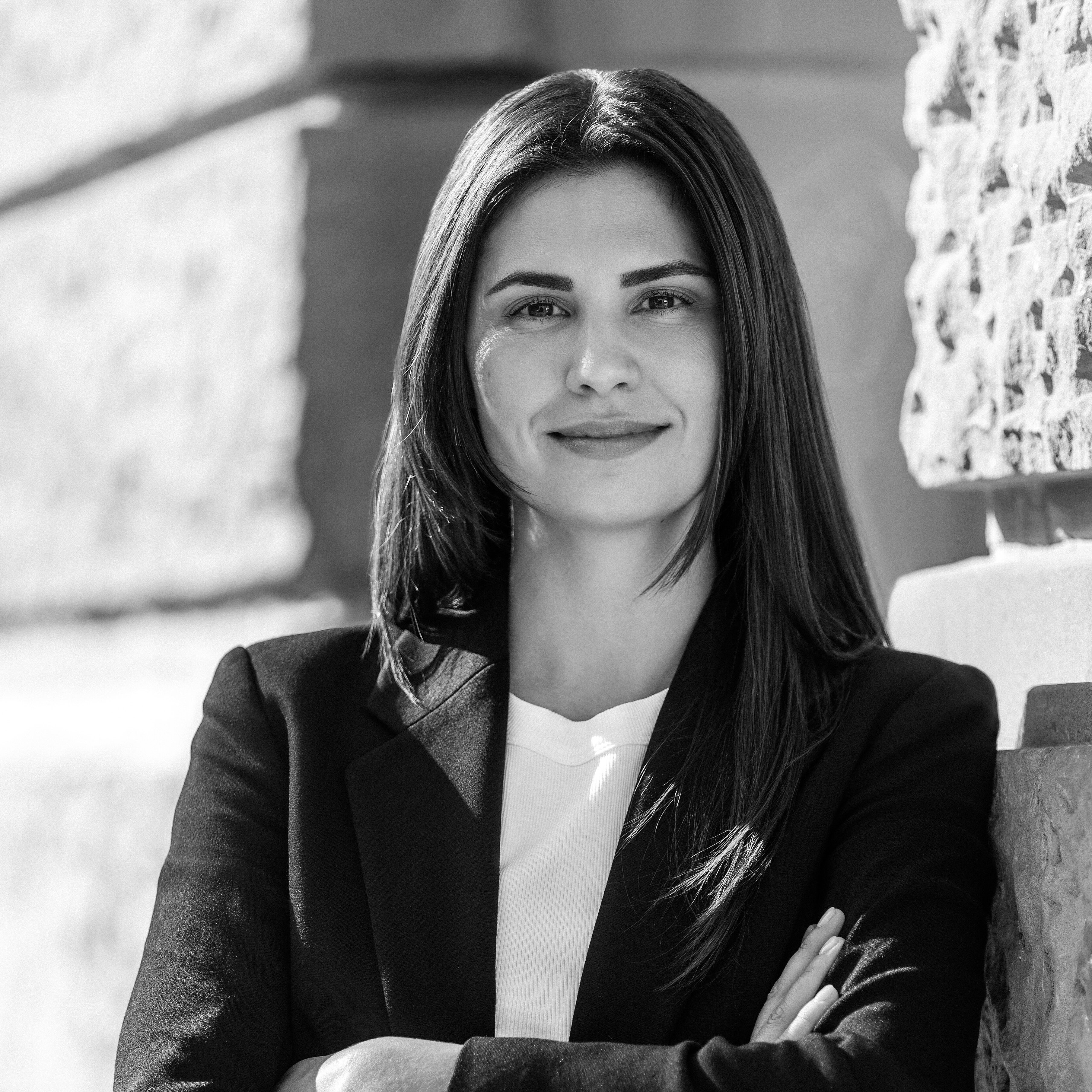 Rechtsanwältin Nadja Müller im dunklen Blazer steht mit verschränkten Armen an einer Steinwand und blickt selbstbewusst in die Kamera