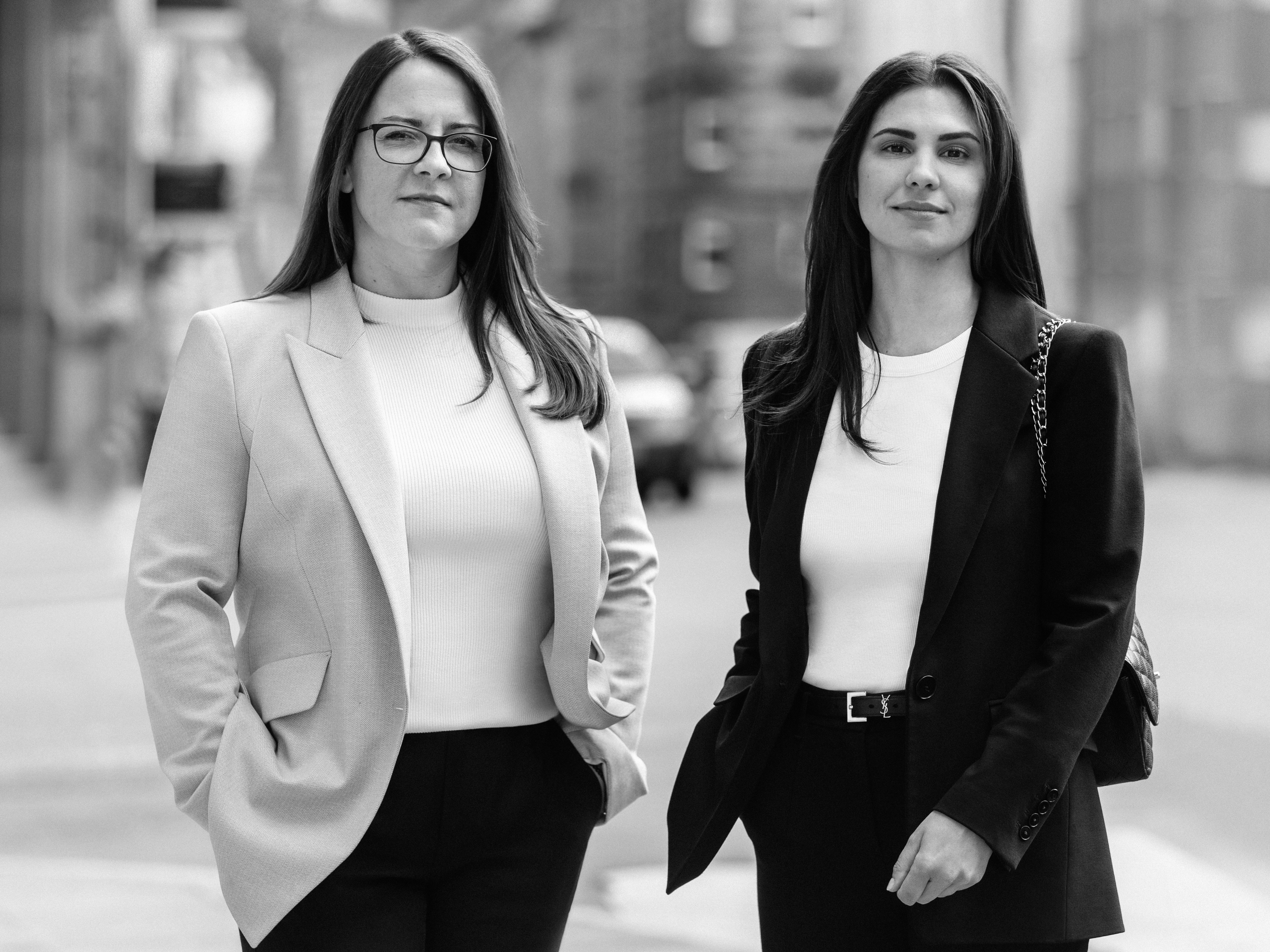 Portrait von Nadja Müller und Melanie Freiin von Neubeck in urbaner Umgebung. Beide Anwältinnen schauen entschlossen in die Kamera.
